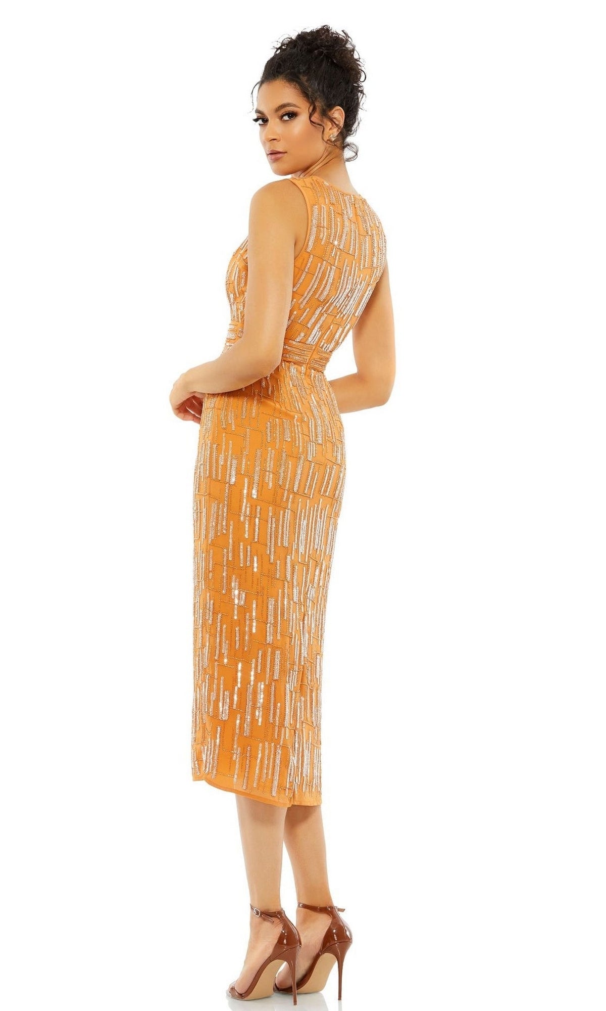 A woman wears the Mac Duggal 70264 Beaded Midi Wedding Guest Dress, a fitted sleeveless orange dress with a geometric pattern, paired with tan heels. Her curly hair is styled up as she looks over her shoulder.